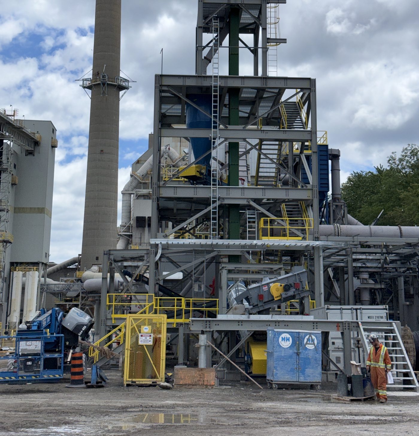 Process plant structure with a stack, steel platforms, ductwork and access stairs, an operator at ground level.