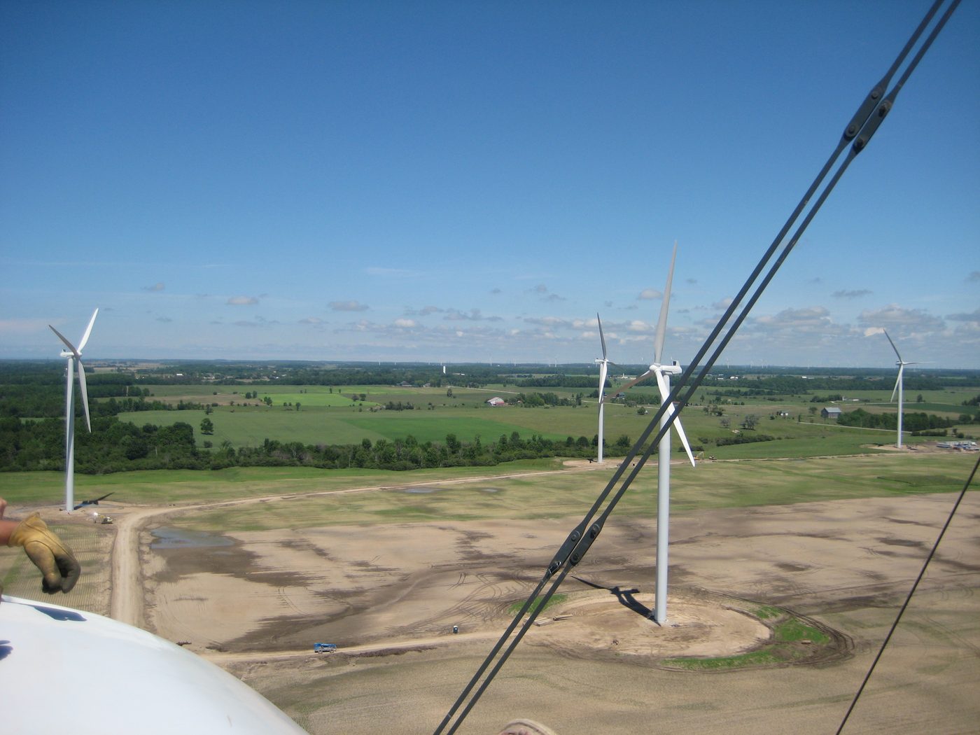 View from a turbine nacelle across a wind farm, with several turbines standing over farmland.